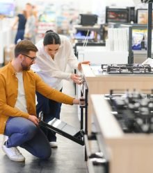 Young man and woman buying new gas stove in appliances shop.
